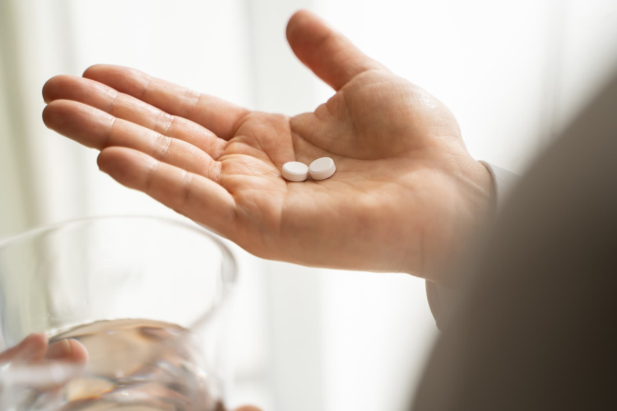 痛み止めをのせた手のひらとコップに入った水