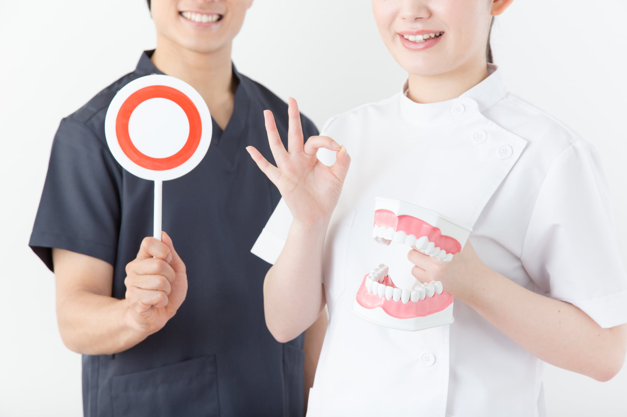 マルの札を持った歯科医と歯の模型を持ち指でOKサインをする歯科衛生士が矯正治療で抜歯を行わないケースの説明をするイメージ